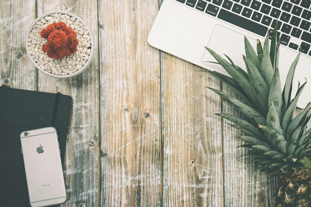 Overhead view of a desk with a laptop, notebook, coffee cup and small plant